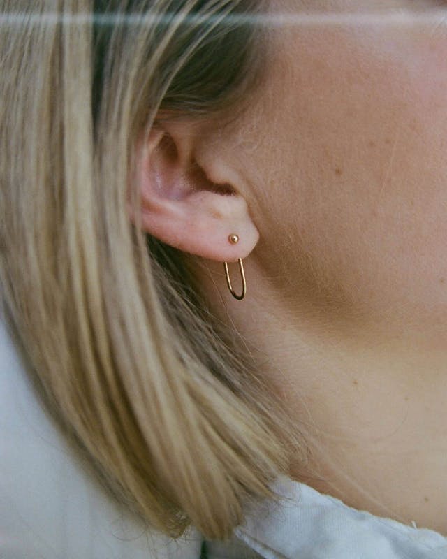Focused photo on blonde woman's ear highlighting the Abel Objects Bend 1 earring.