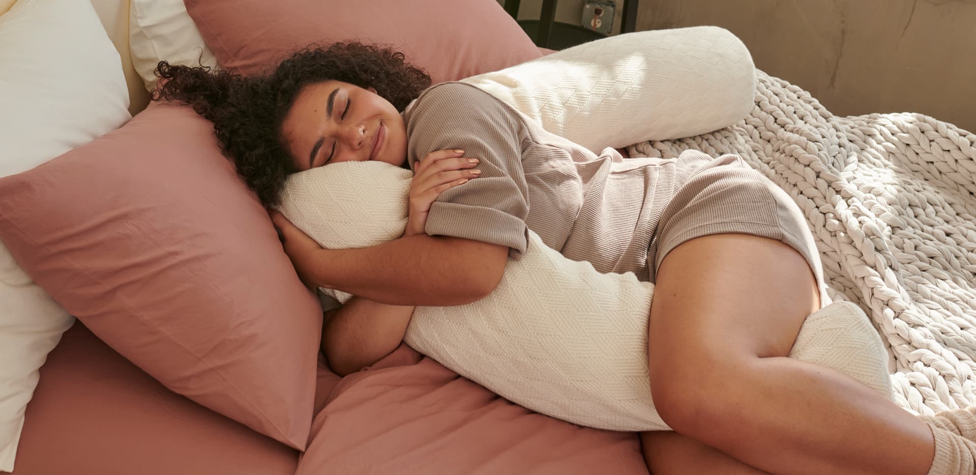 Woman cuddling with a Bearaby product whlie sleeping on a bed.