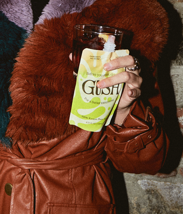 Close up photo of a person in a dark red jacket holding a Gush drink pouch.